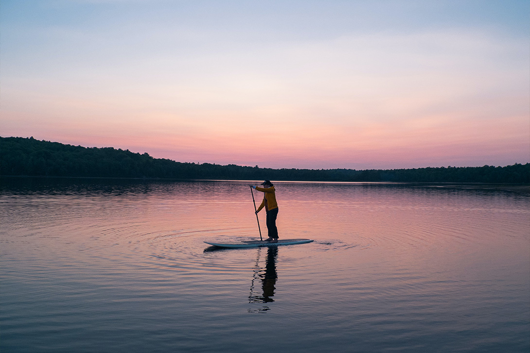 person paddle boarding in a lake during pink sunset